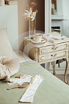 Vintage accessories on the bed and bedside table. Boho style. Gloves, cup and mirror