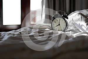 Vintage Alarm clock on bedroom in the morning with sunlight at the windows background. Sleeping in winter or autumn season concept