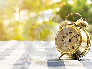 Vintage alarm clock on blue plaid tablecloth. The background is green from tree