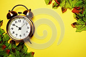 Vintage Alarm Clock and Green Maple Leaves over on yellow Background