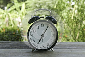 A vintage alarm clock on a wooden table on a bright sunny day with a nature background