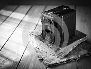 Vintage analogue film camera on a wooden table, old book, clothl. Black and white photo. Copy space
