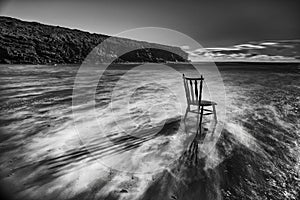 Vintage antique chair tucked into the water of an Irish beach surrounded by rocks and cliffs. long exposure with traces of water.