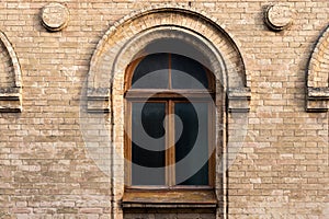 Vintage arched window in the wall of yellow brick. Black glass in a maroon dark red wooden frame. The concept of antique