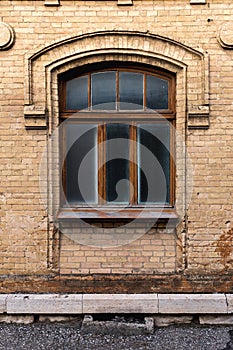 Vintage arched window in the wall of yellow brick. Black glass in a maroon dark red wooden frame. The concept of antique