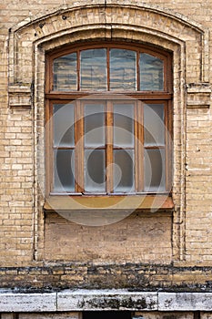 Vintage arched window in the wall of yellow brick. Black glass in a maroon dark red wooden frame. The concept of antique