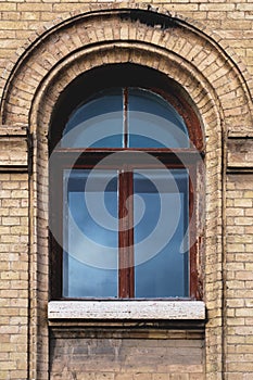 Vintage arched window in the wall of yellow brick. Black glass in a maroon dark red wooden frame. The concept of antique