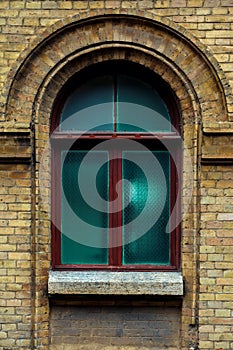 Vintage arched window in the wall of yellow brick. Green - the colors of sea wave glass in a maroon dark red wooden