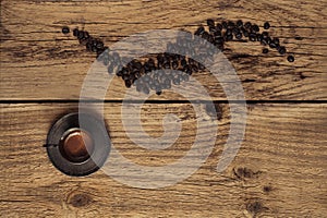 Vintage background with coffee beans arranged in a pattern and a silver espresso cup on wooden table.