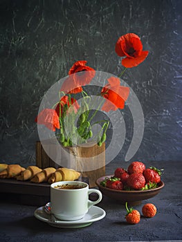 Vintage background with red poppies in a wooden vase, a cup of coffee, strawberries in a plate and croissants on a wooden tray
