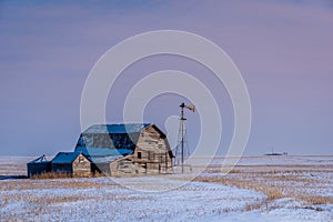 Vintage barn, bins and windmill surrounded by snow under pink sunset sky in Saskatchewan
