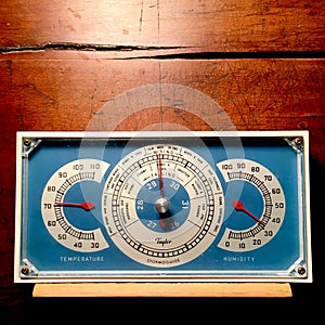 Vintage barometer with thermometer and hygrometer, shown against a weathered wood background.