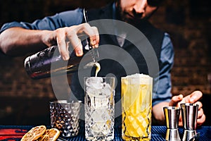 Vintage bartender pouring fresh orange vodka cocktail over ice in crystal glassware