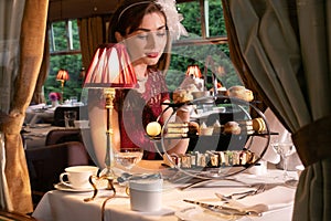 Vintage, beautiful woman in red dress enjoying afternoon tea in train carriage with cakes, sandwiches and tea