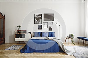 Vintage bedroom interior with bedside table, king size bed with blue bedding and pillows. Mockup gallery on the white wall