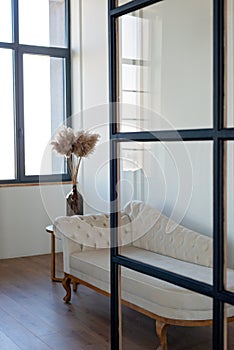 Vintage beige sofa in velor upholstery in a modern interior, with a vase of dried flowers. Interior design. Soft selective focus