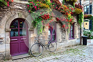 Vintage bicycle in front of the old rustic house, covered with flowers. Beautiful city landscape with an old bike near the stone