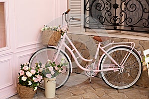 Vintage bike with basket with bouquet flowers of roses stands near cafe of bakery. Eco transport. pink bicycle with flower pots wi