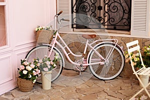 Vintage bike with basket with bouquet flowers of roses stands near cafe of bakery. Eco transport. pink bicycle with flower pots wi