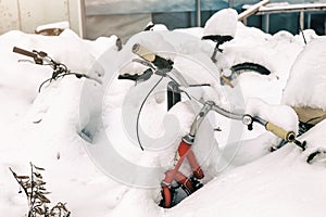 Vintage bike covered with big thick snow layer after blizzard at european city street in winter. Abandoned bicycle buried in