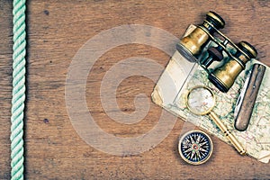 Vintage binoculars, compass, old map, magnifying glass, pocket knife, rope on wooden background