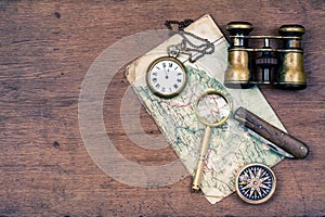 Vintage binoculars, compass, old map, magnifying glass, pocket watches, knife on wooden desk background