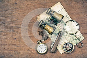 Vintage binoculars, compass, old map, magnifying glass, pocket watches, knife on wooden table background
