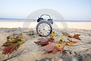 Vintage black alarm clock on autumn leaves. Time change abstract photo