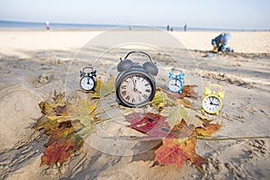 Vintage black alarm clock on autumn leaves. Time change abstract photo