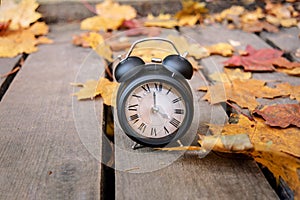 Vintage black alarm clock on autumn leaves. Time change abstract photo