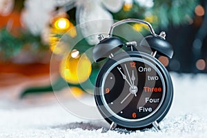 Vintage black alarm clock on snow on blur background of Christmas tree. New Year Theme
