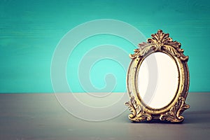 Vintage blank gold photo frame over wooden table. Ready for photography montage.