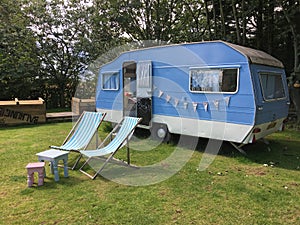 Vintage blue caravan, deck chairs and tables on grass