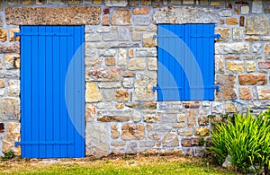 Vintage blue door and window on the facade of an old cottage stone wall.