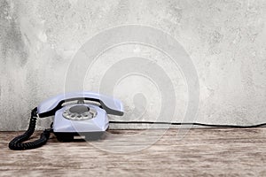 Vintage blue rotary dial telephone on wooden table in front gray concrete wall