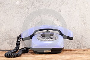 Vintage blue rotary dial telephone on wooden table in front gray concrete wall