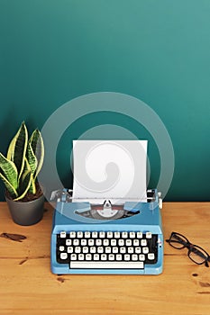 Vintage blue typewriter on a wooden desk against a dark green wall.