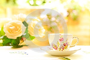 Vintage bone china tea cup and saucer set and white roses on a bright sunny day in the garden