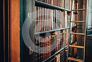 Vintage books in leather covers on bookshelf cabinet with ladder.