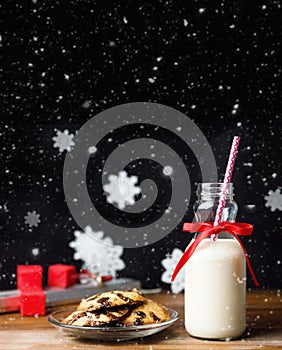 Vintage bottle of milk with red ribbon and santas cookies on wooden table over black background