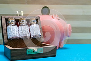 Vintage Bottles of homeopathic pills in old wooden box and Indian coin on pink piggy bank on blue surface and dark background -