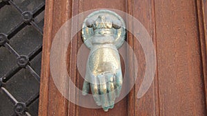 Vintage brass door knocker in the form of a hand with a ring on the finger on an old door