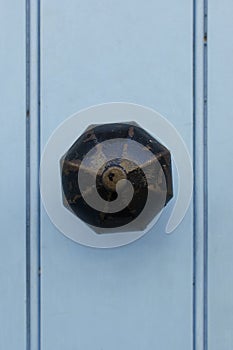 Vintage brass doorknob with worn black paint on light blue wooden door