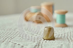 Vintage brass thimble close-up.  It is on an old handmade knitted tablecloth.  In the background vintage wooden bobbins with