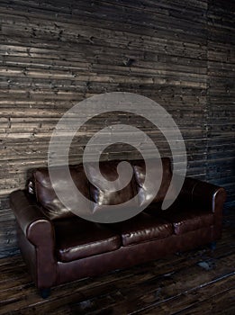 Vintage brown leather sofa on a wooden wall and floor