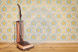 Vintage brown vacuum cleaner in a room with floral wallpaper and wooden floor