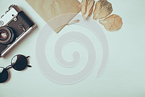 Vintage camera with dried leaves with craft paper envelope on a wooden white background