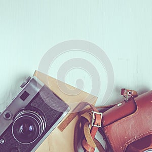 Vintage camera with leather case and craft paper envelope on a wooden white background. Copy space. square format, toned