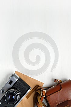 Vintage camera with leather case and craft paper envelope on a wooden white background. Copy space. Vertical. Toned