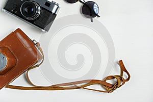 Vintage camera with leather case and sunglasses on a wooden white background